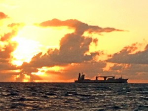 The sun explodes behind the clouds as a ship passes us to starboard.